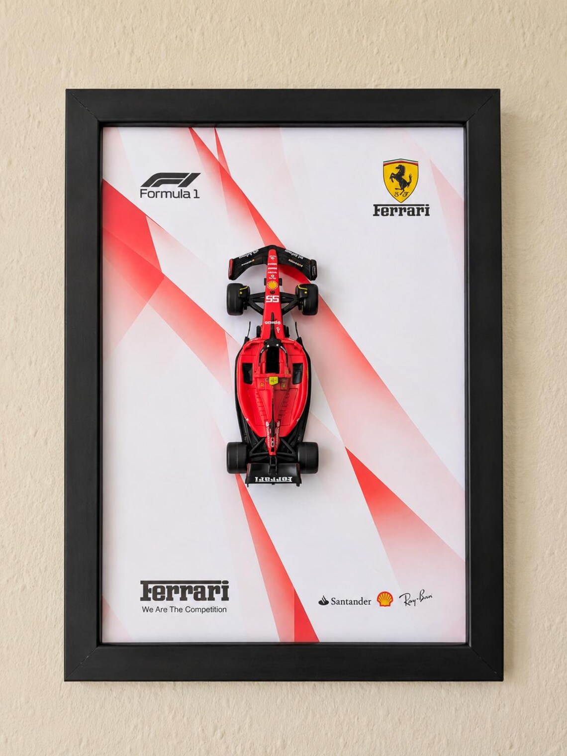 Front view of a red Formula 1 Ferrari model mounted vertically in a black frame against a red and white background.