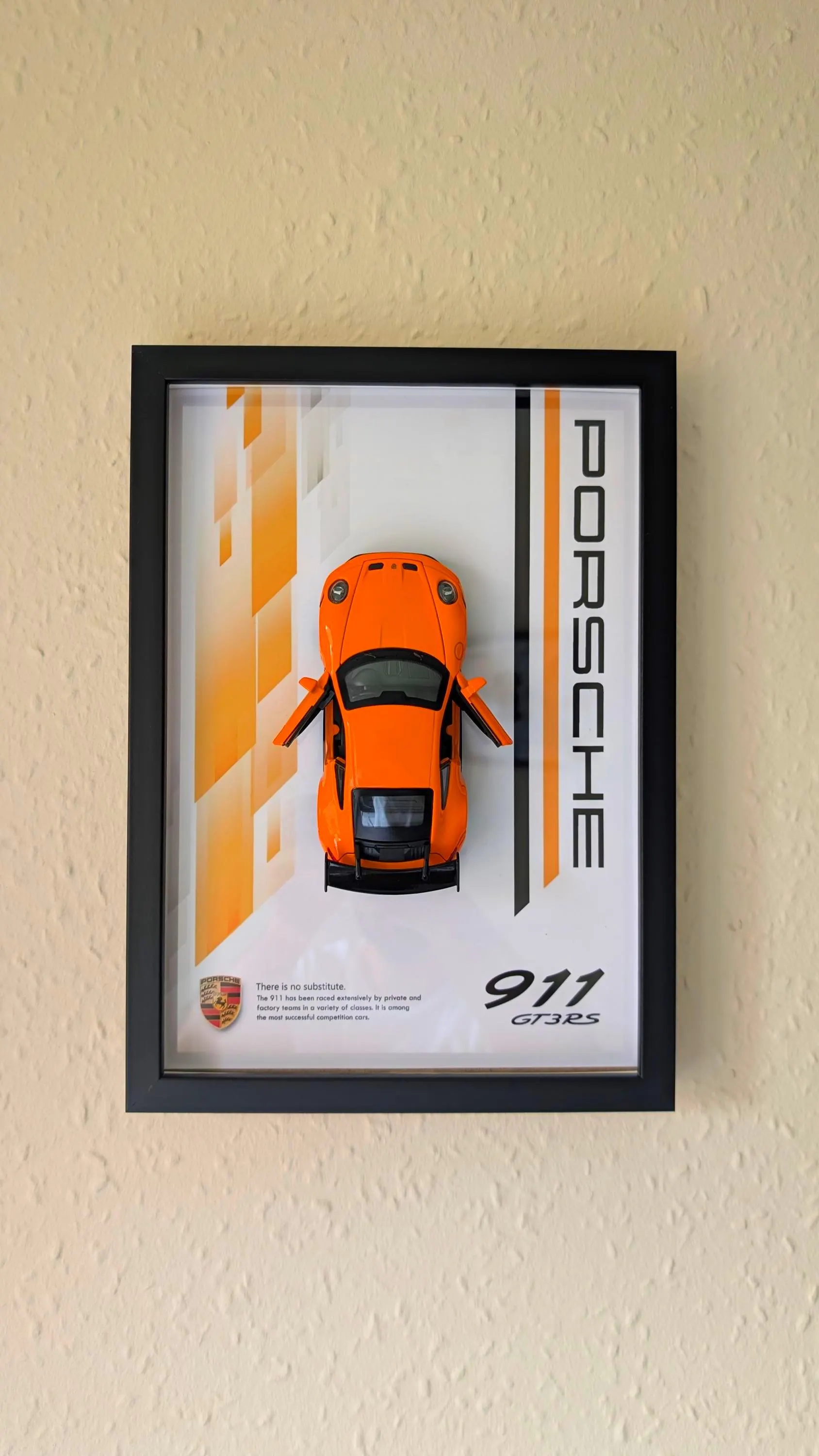 Orange 1:32 Porsche 911 GT3 RS diecast car in a black A4 shadow box frame hanging on a wall